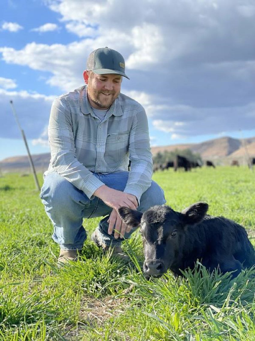 A Man Kneeling Next to a Black Calf.